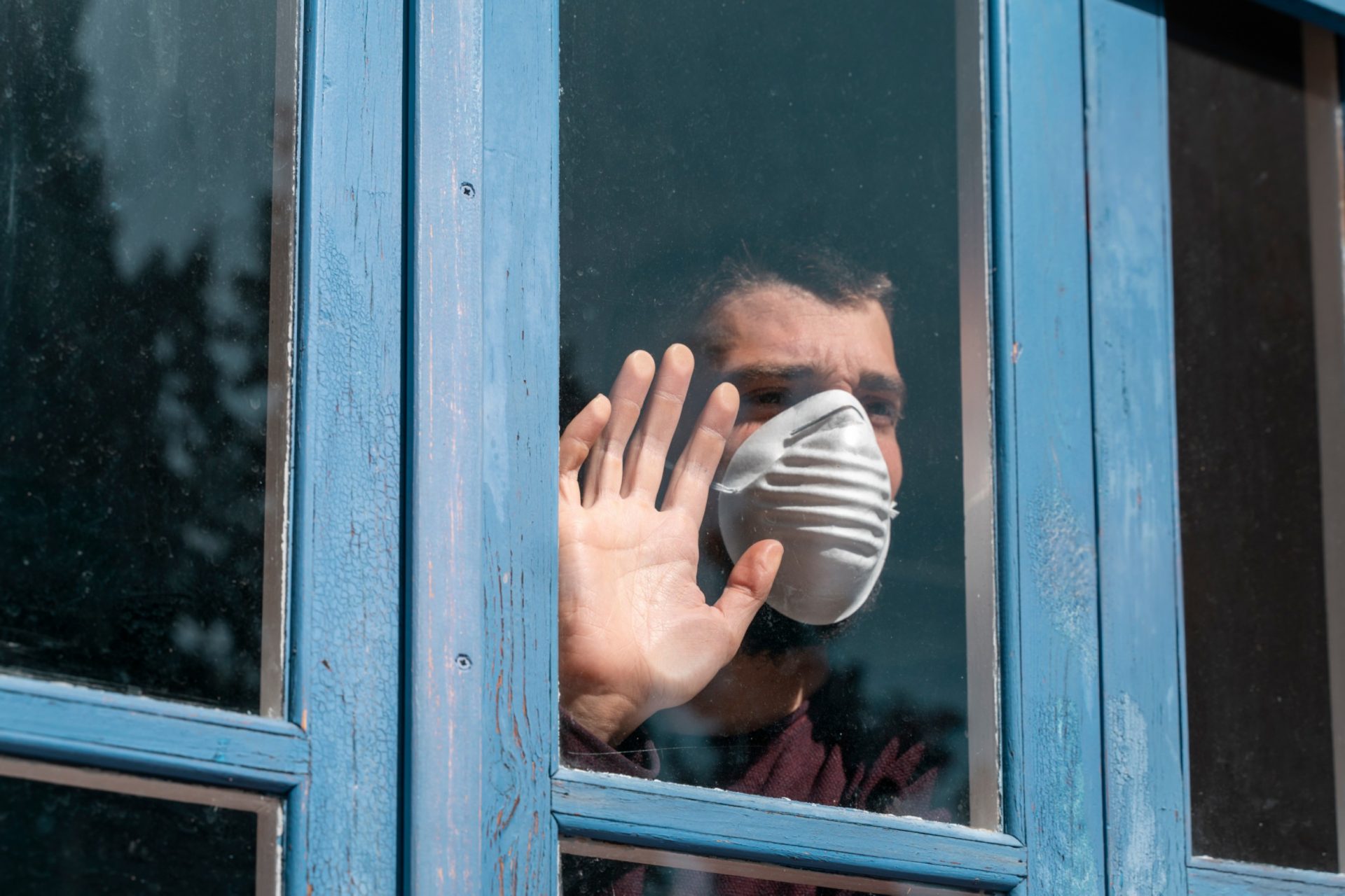 mladić sa maskom gleda kroz prozor